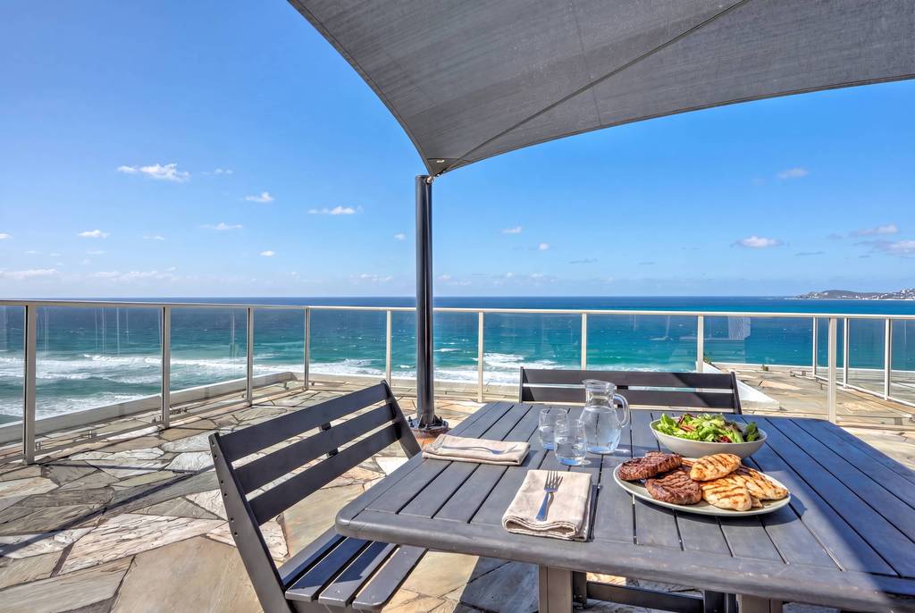 Dining table and benches on rooftop terrace with ocean beyond